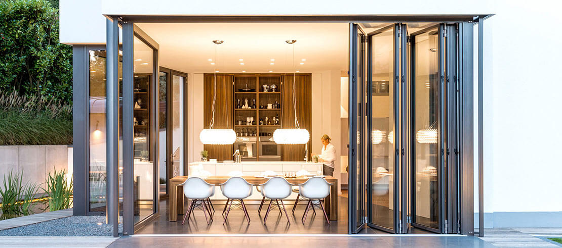 Geopend Highline Aluminium vouwglas met zicht van buitenaf op de verlichte keuken