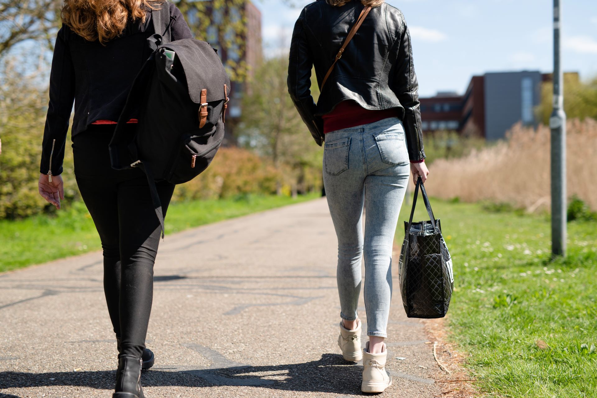 Twee vrouwen lopen samen over een pad in een groene omgeving, gezien van achteren, met tassen bij zich.