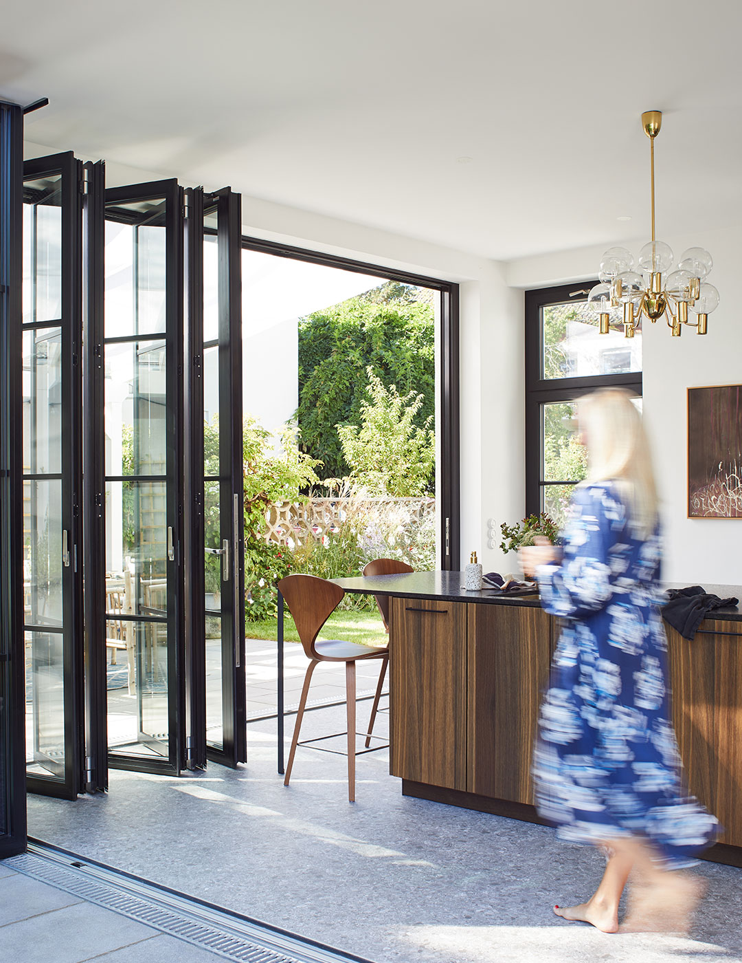 Frau geht durch geöffnete Glas-Faltwände von der Küche in den Garten