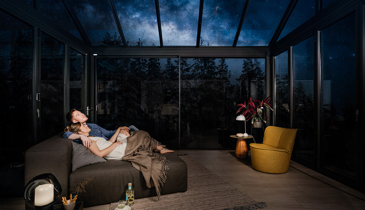 Ett par som sitter i soffan i en vinterträdgård sett inifrån på natten.
