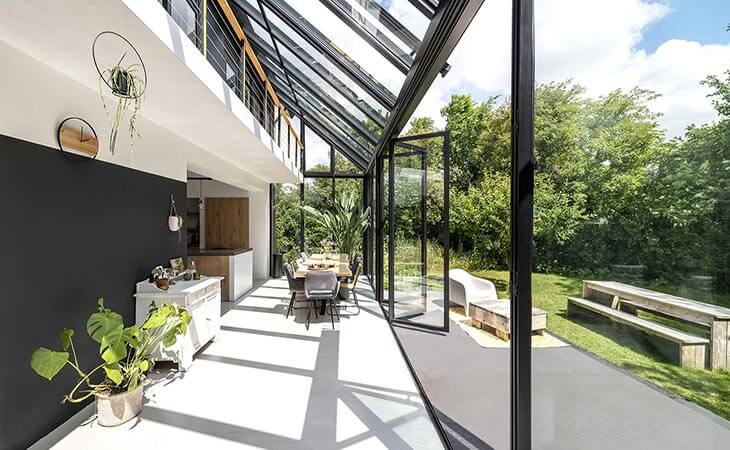 Aflang vinterhave over to etager, hvor den nederste er indrettet med spisebord og planter, og den øverste er en indendørs terrasse med udsigt udover haven.