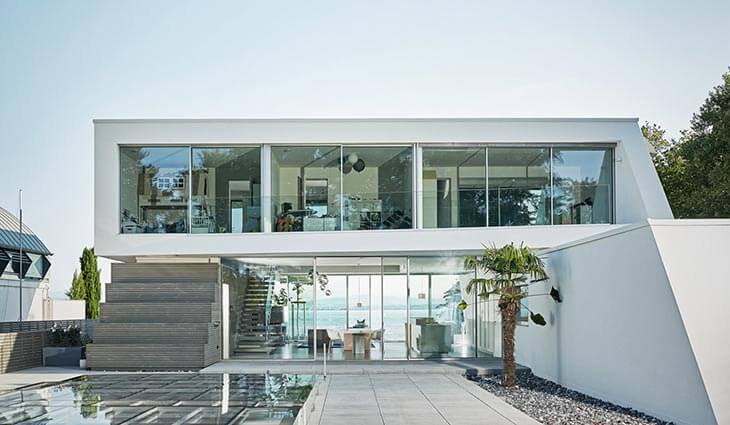 CERO skydedør installeret i et stor hvidt og moderne hus, som har udgang til udsigt ud over vand på den ene side og udgang til pool og terrasseareal på den anden side. Skydedøren er placeret i stue-etage, hvorfra der haves udsigt ud til begge sider af huset.