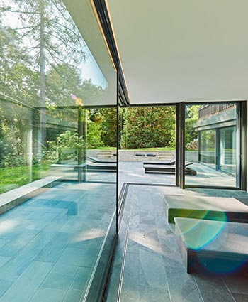 CERO Skydedørssystem med store glaspartier, som giver adgang til husets udeareal, som inkluderer terrasse med loungeområde og græsareal. Indendørs ses to daybeds.