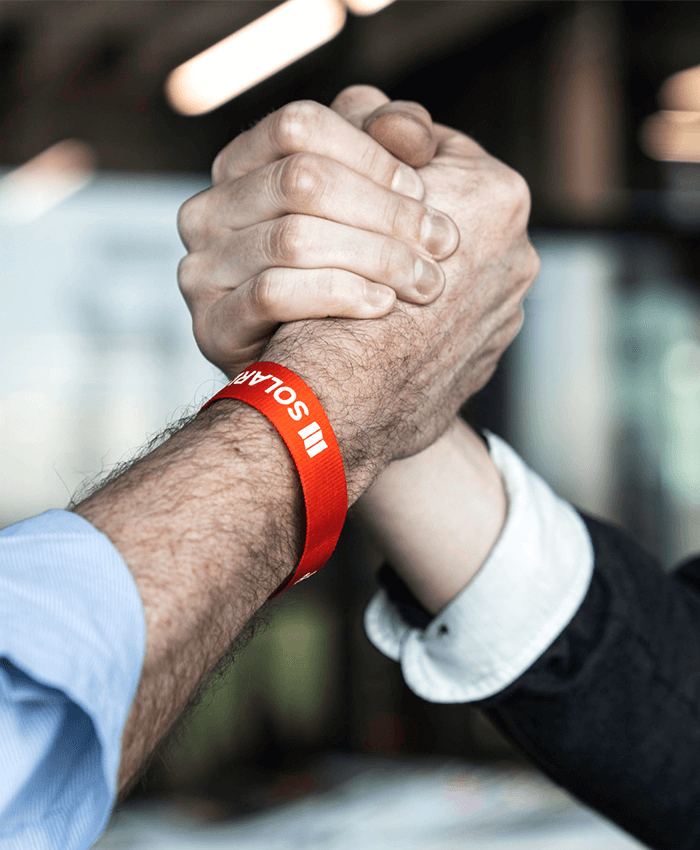 Zwei Personen geben sich einen Handschlag, eine Person trägt ein Solarlux Armband