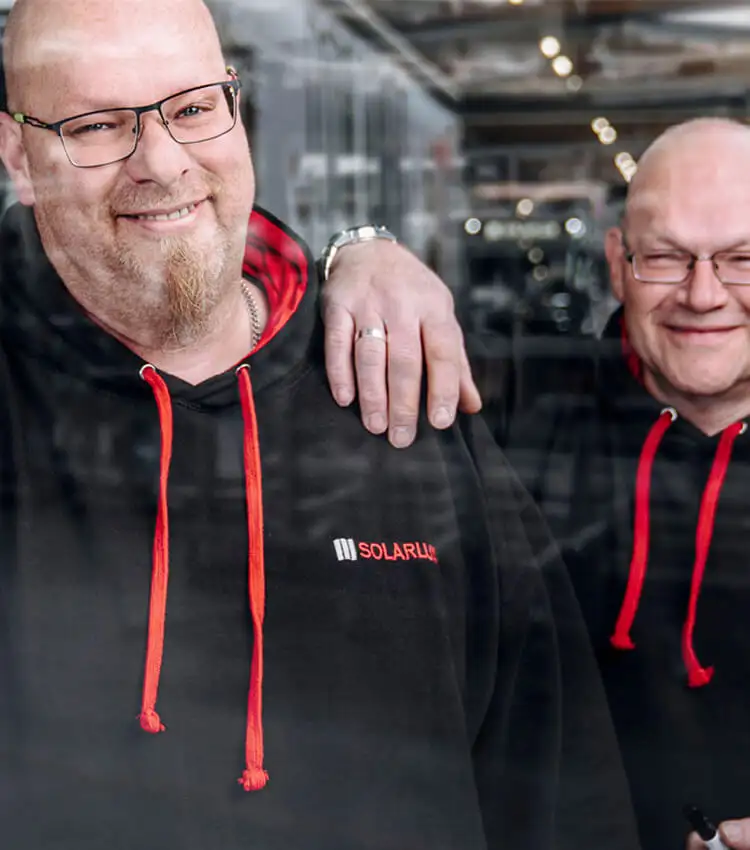 Zwei Männer stehen vor einem LKW und lächeln