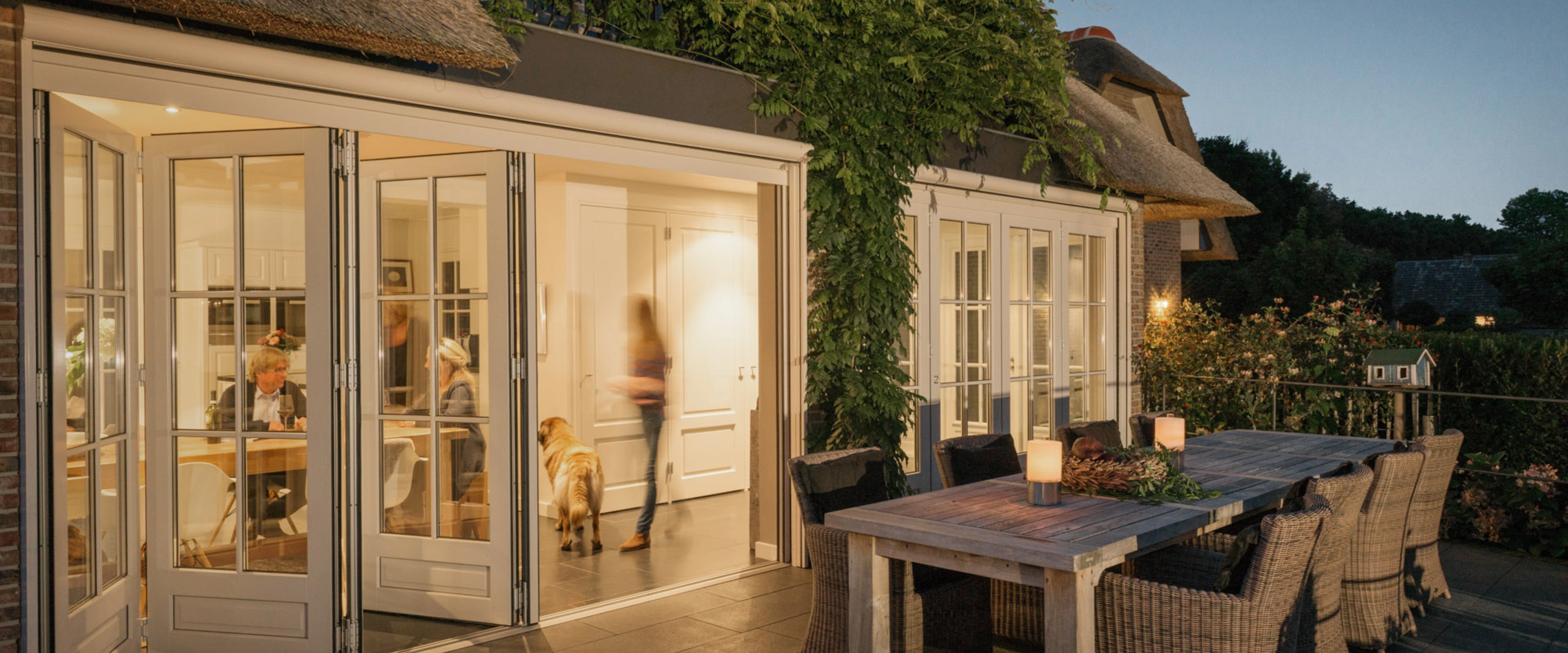 Foldedør fra Solarlux med udgang til terrasse, om aftenen i en hyggelig sommerhushave