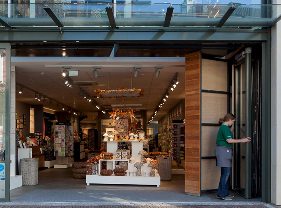 Frau öffnet Glas Faltwand verbaut im Geschäftseingang