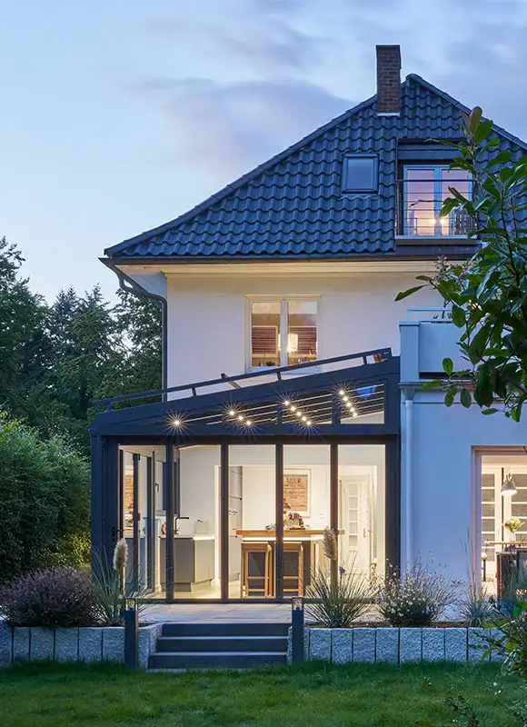 Blick aus dem Garten auf einen beleuchteten Wintergarten