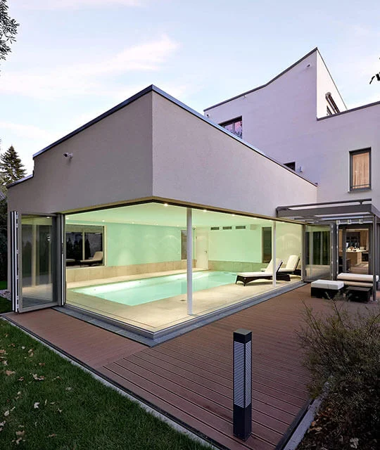 Een groot huis met een overdekt zwembad en vouwdeuren naar buiten.