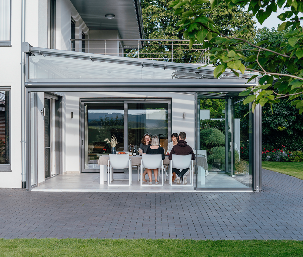 Venner, der spiser middag i en moderne glasinddækket terrasse med spiseplads. 