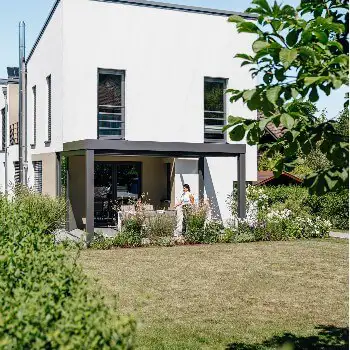 terrasseoverdækning fra Solarlux i aluminium og er modellen SDL Acubis, som er placeret i forlængelse af moderne hvidt hus med udsigt ud over haven.