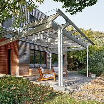 SDL Aura terrasseoverdækning i trø og aluminium med glastag og åbne sider.