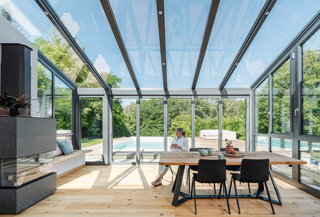 kvinde sidder ved spisebordet i en glasinddækket terrasse. 