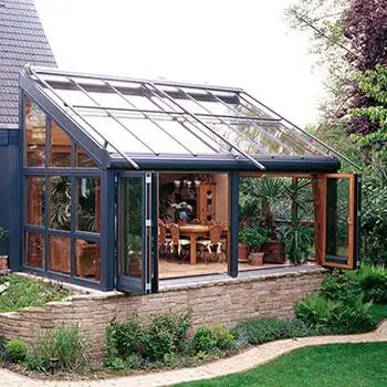 SDL Avantgarde vinterhave med konstruktion i træ og aluminium og med foldedør, som åbner op til udeareal. Vinterhaven har varmeisoleret glastag og glasvægge, hvilket giver mulighed for masser lys til vinterhavens areal, som er indrettet med spisebord og planter.