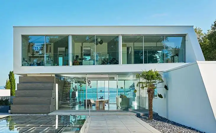 Smukt hvidt og moderne hus med pool, udsigt til havet og et skydedørssystem i underetagen, som giver adgang til begge dele af huset og flot udsigt ud over vandet samt nem adgang til pool.