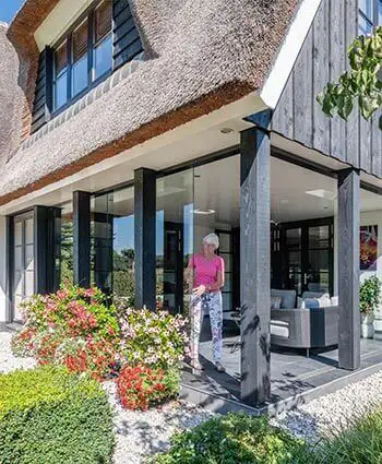 Skydedør på et klassisk stråtagshus med lodrette stolper, som åbner op til et bed med perlegrus. Skydedørens inderside er placeret på en delvist åben terrasse, som dog er overdækket af huset anden etage.